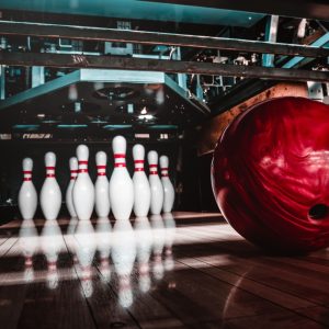 A red bowling ball rolls towards ten bowling pins at the end of a lane